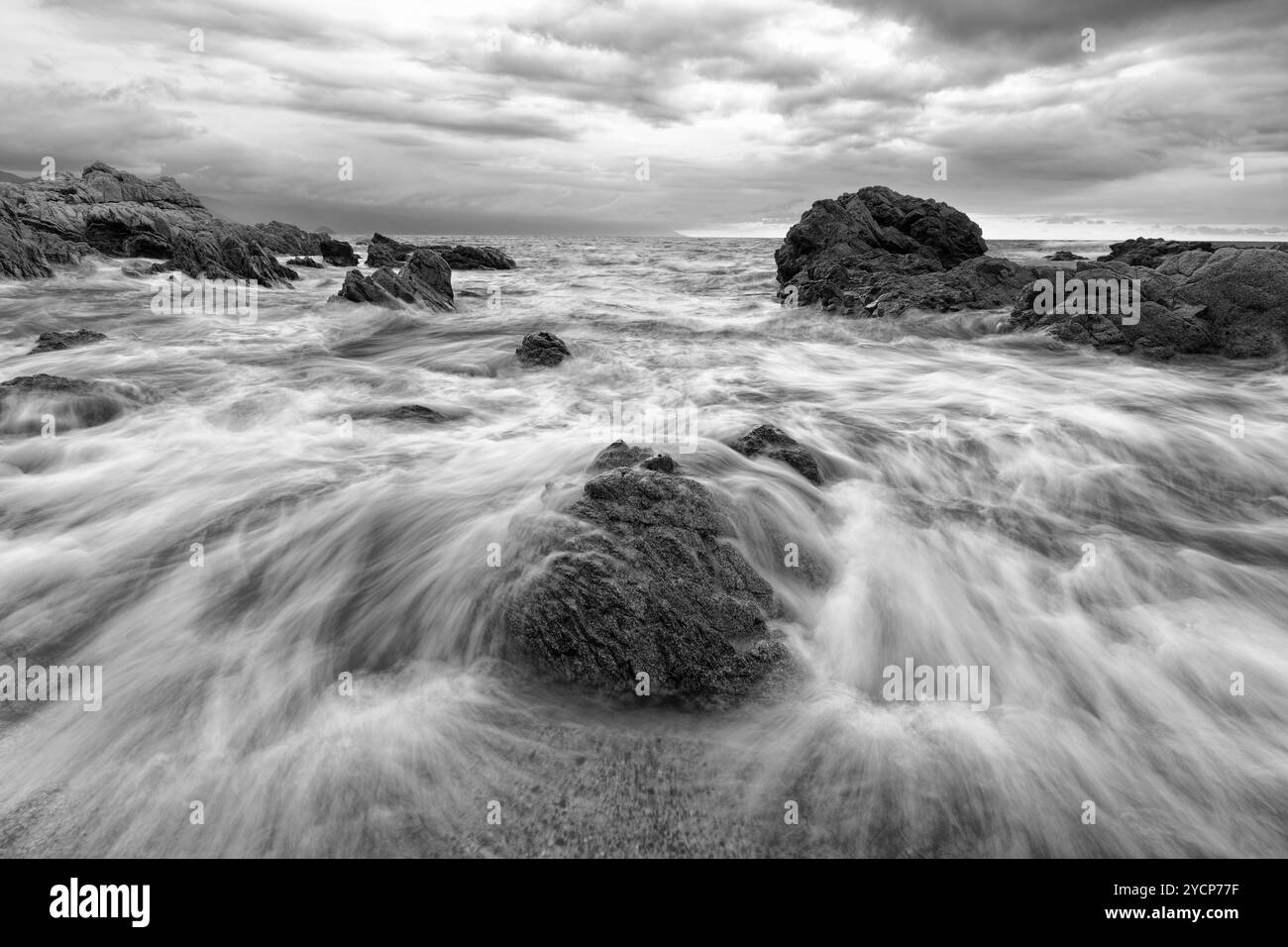 Une vague se brise avec de l'eau coulant au-dessus des rochers dans Une image spectaculaire de paysage marin en noir et blanc Banque D'Images