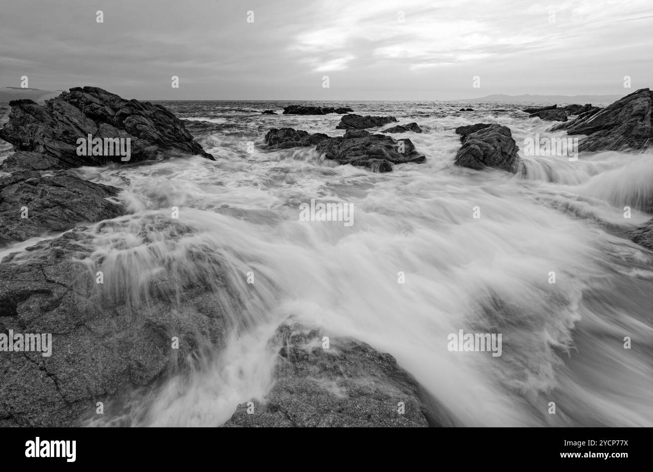 Une vague se brise avec de l'eau coulant au-dessus des rochers dans Une image spectaculaire de paysage marin en noir et blanc Banque D'Images