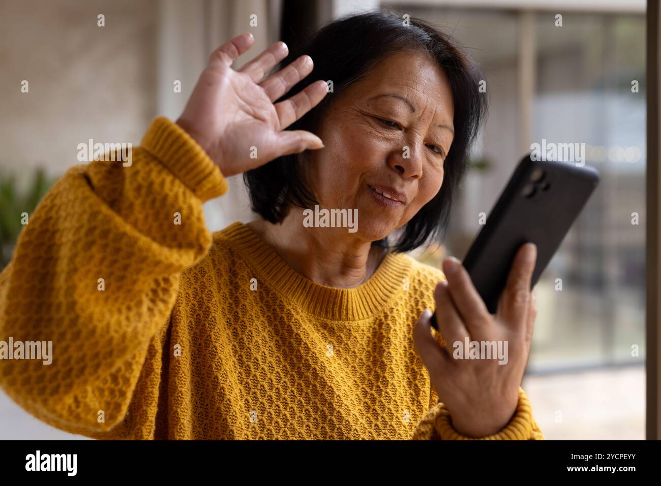 femme senior asiatique discutant sur smartphone, souriant chaleureusement à la maison Banque D'Images