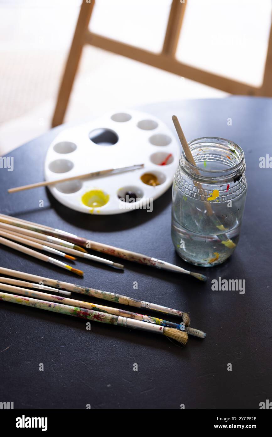 Fournitures d'art sur table avec pinceaux, palette, et pot d'eau, à la maison Banque D'Images