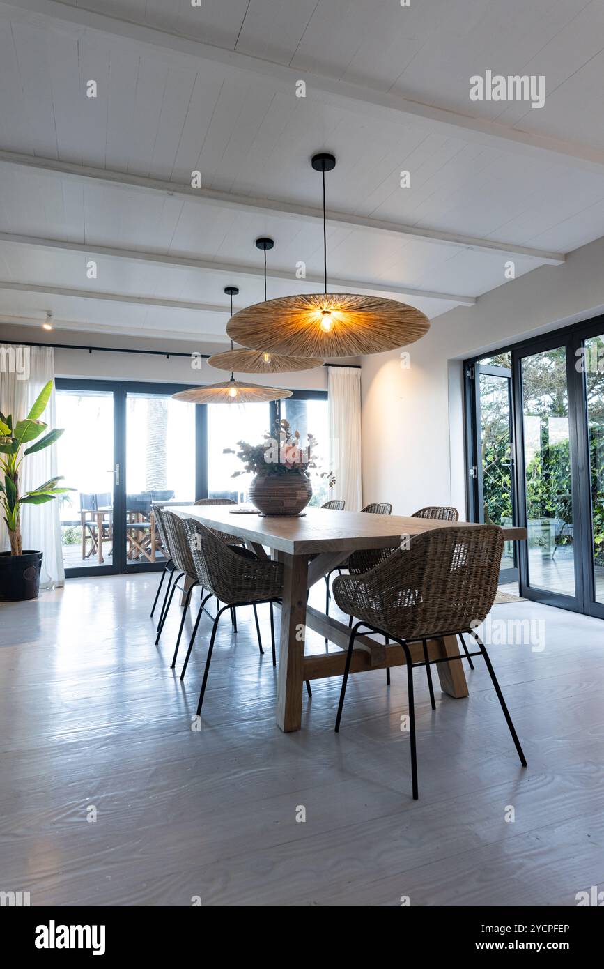 À la maison, salle à manger moderne avec des chaises en osier et de grandes fenêtres, créant une ambiance chaleureuse Banque D'Images