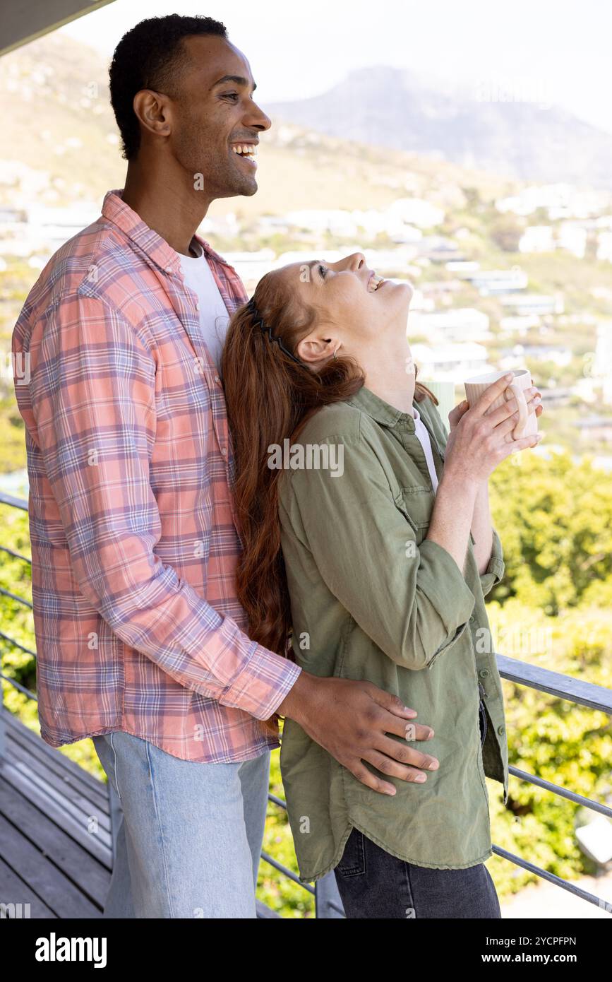 Couple multiracial profitant du café du matin sur le balcon, riant et embrassant joyeusement Banque D'Images Couple multiracial profitant du café du matin sur le balcon, riant et embrassant joyeusement Banque D'Images