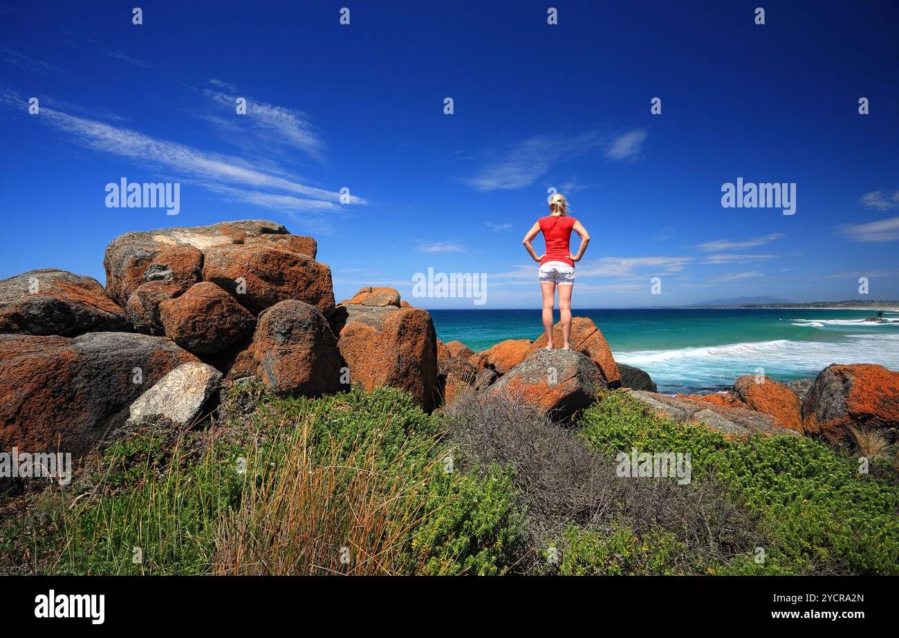 Une femelle debout sur les rochers oranges vibrants et regardant vers la mer. Bingie point, parc national Eurobodalla sur la Sapphire Coast de Nouvelle-Galles du Sud, Australie Banque D'Images