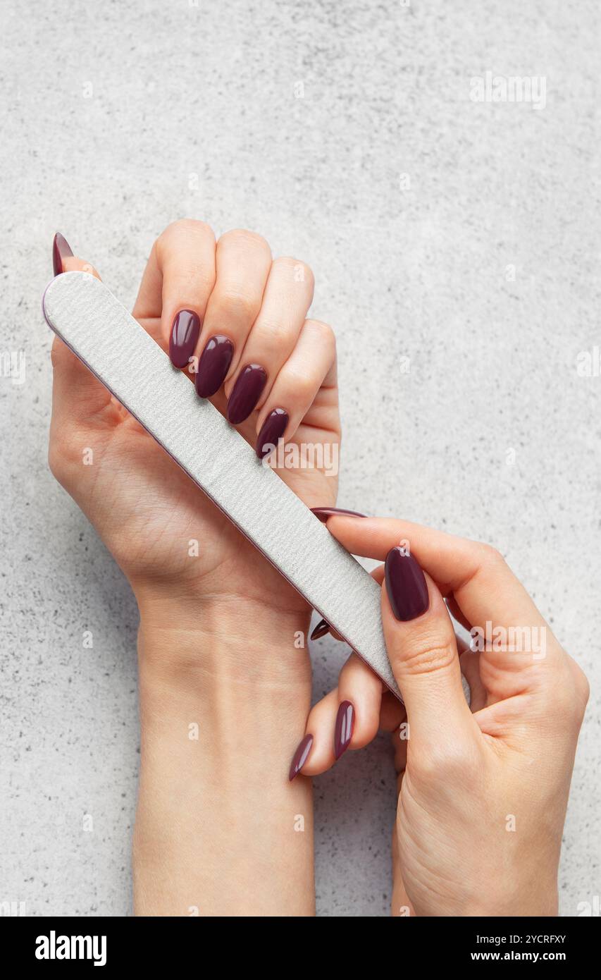 Une personne remplit soigneusement ses ongles à la maison, en utilisant une lime à ongles pour façonner et lisser les bords, créant un look élégant pour une manucure. Banque D'Images