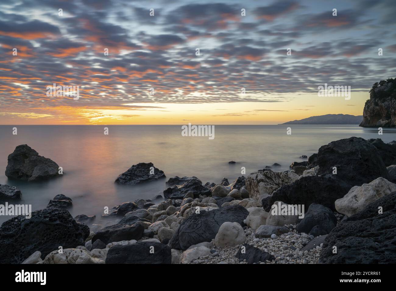 Un lever de soleil coloré à la plage de Cala Gonone avec des rochers noirs et blancs et des rochers au premier plan Banque D'Images