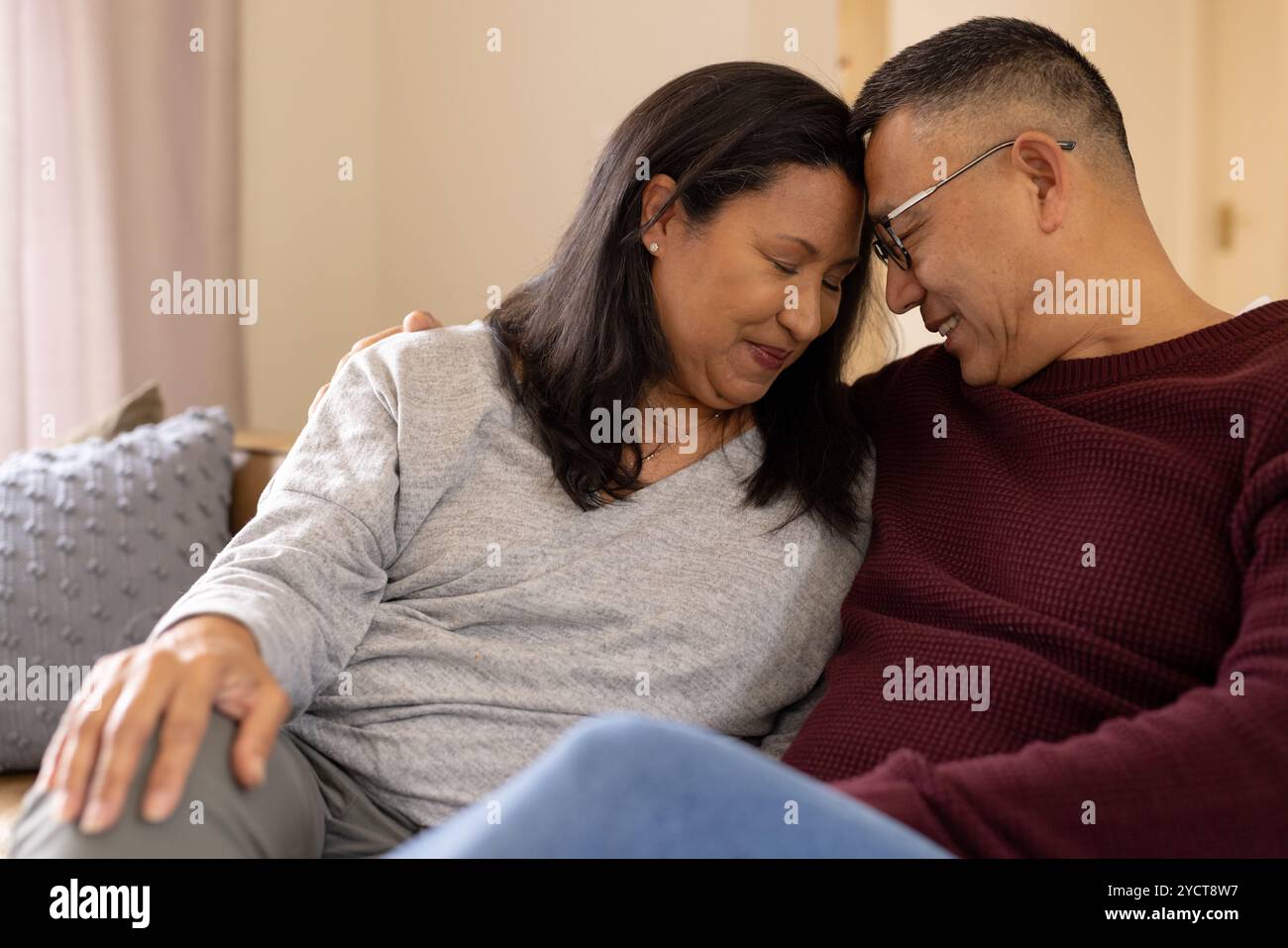 Couple senior multiracial partageant un moment tendre à la maison, embrassant et souriant chaleureusement Banque D'Images