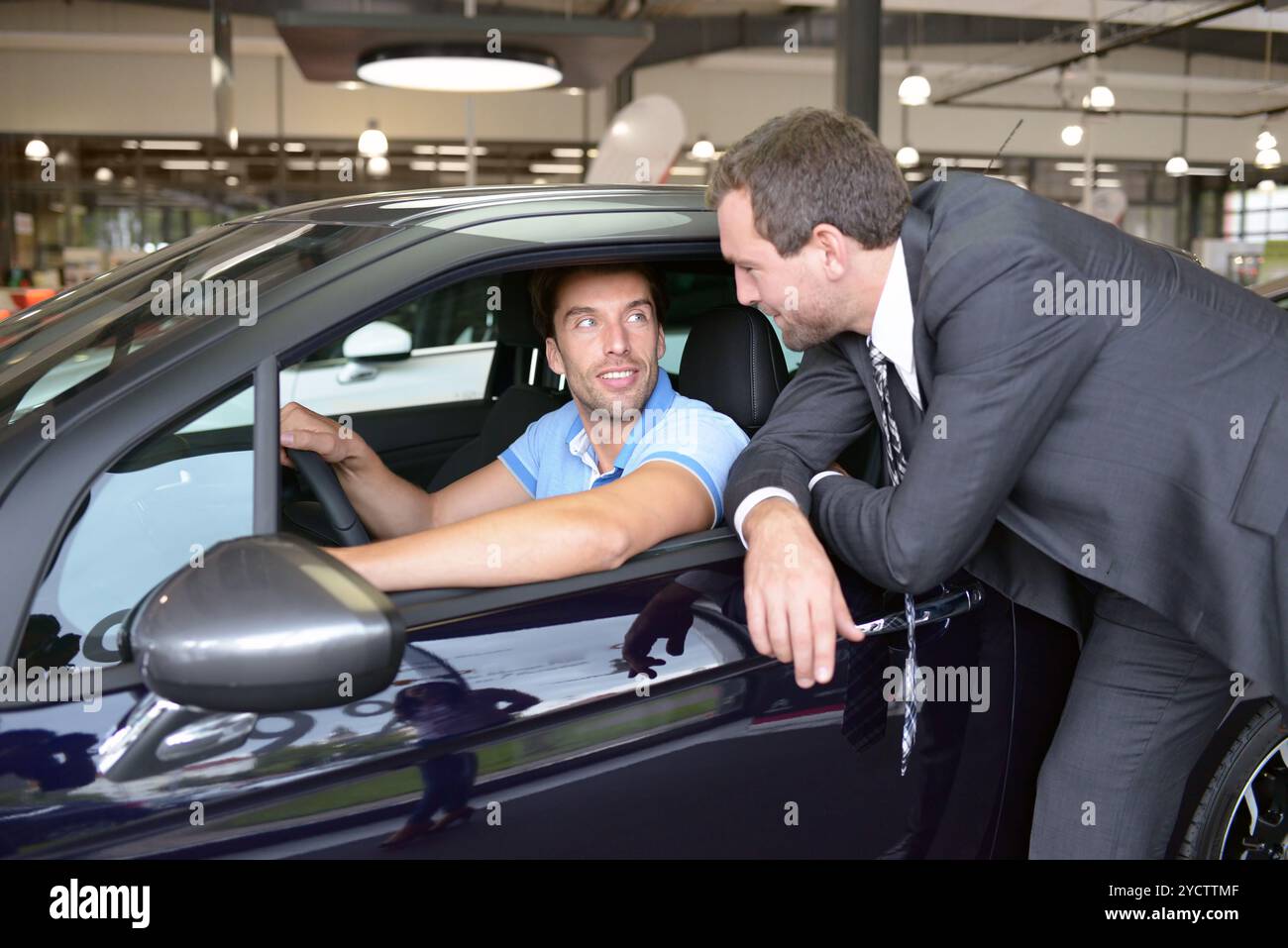 Conseils dans la concession automobile - vendeur et jeune homme vendant une nouvelle voiture Banque D'Images