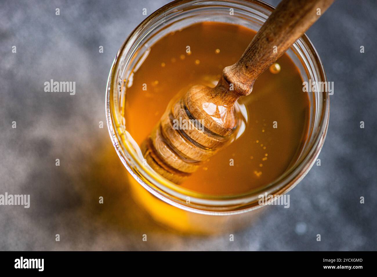D'en haut scintillement du miel organique coulant d'une benne en bois dans un bocal en verre placé sur un fond neutre. Les tons dorés chauds et collants t Banque D'Images