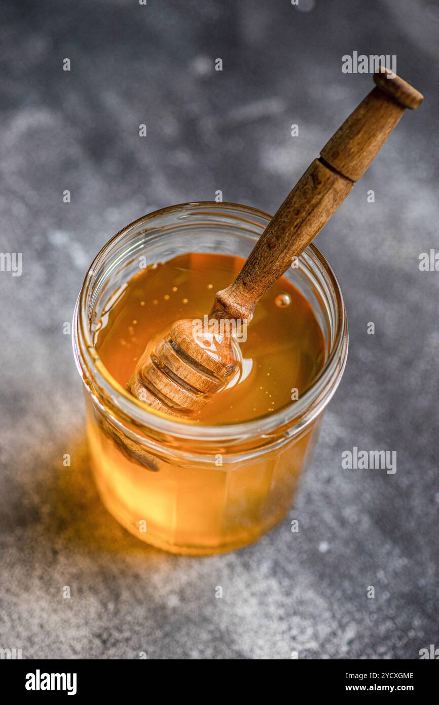 Par le haut, le miel organique coule d'une benne en bois dans un bocal en verre, capturé sur une surface texturée. Banque D'Images