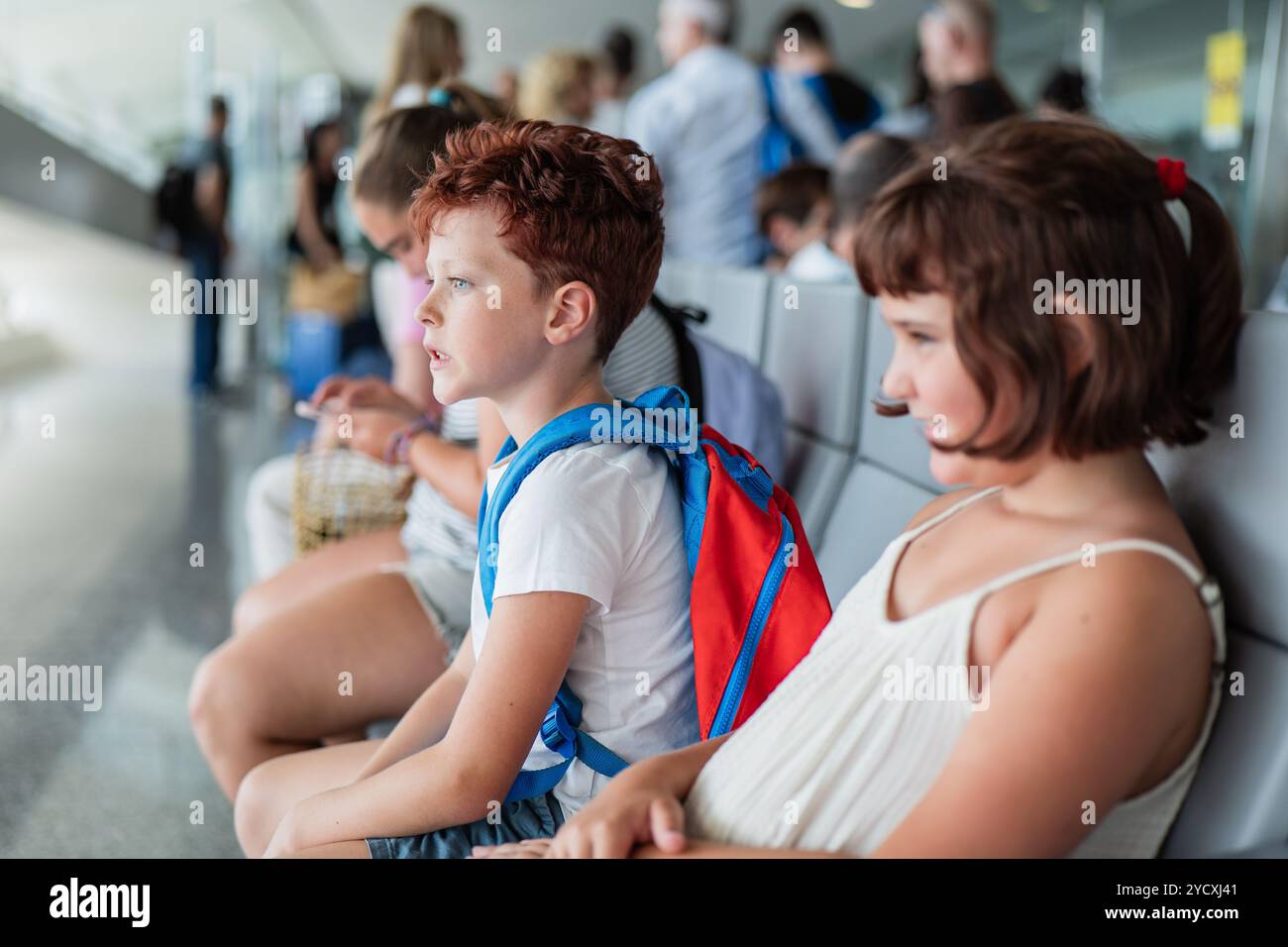 Deux enfants, un garçon et une fille, assis patiemment dans un terminal d'aéroport. Le garçon, aux cheveux roux, regarde intentionnellement quelque chose hors cadre, tandis que la fille Banque D'Images
