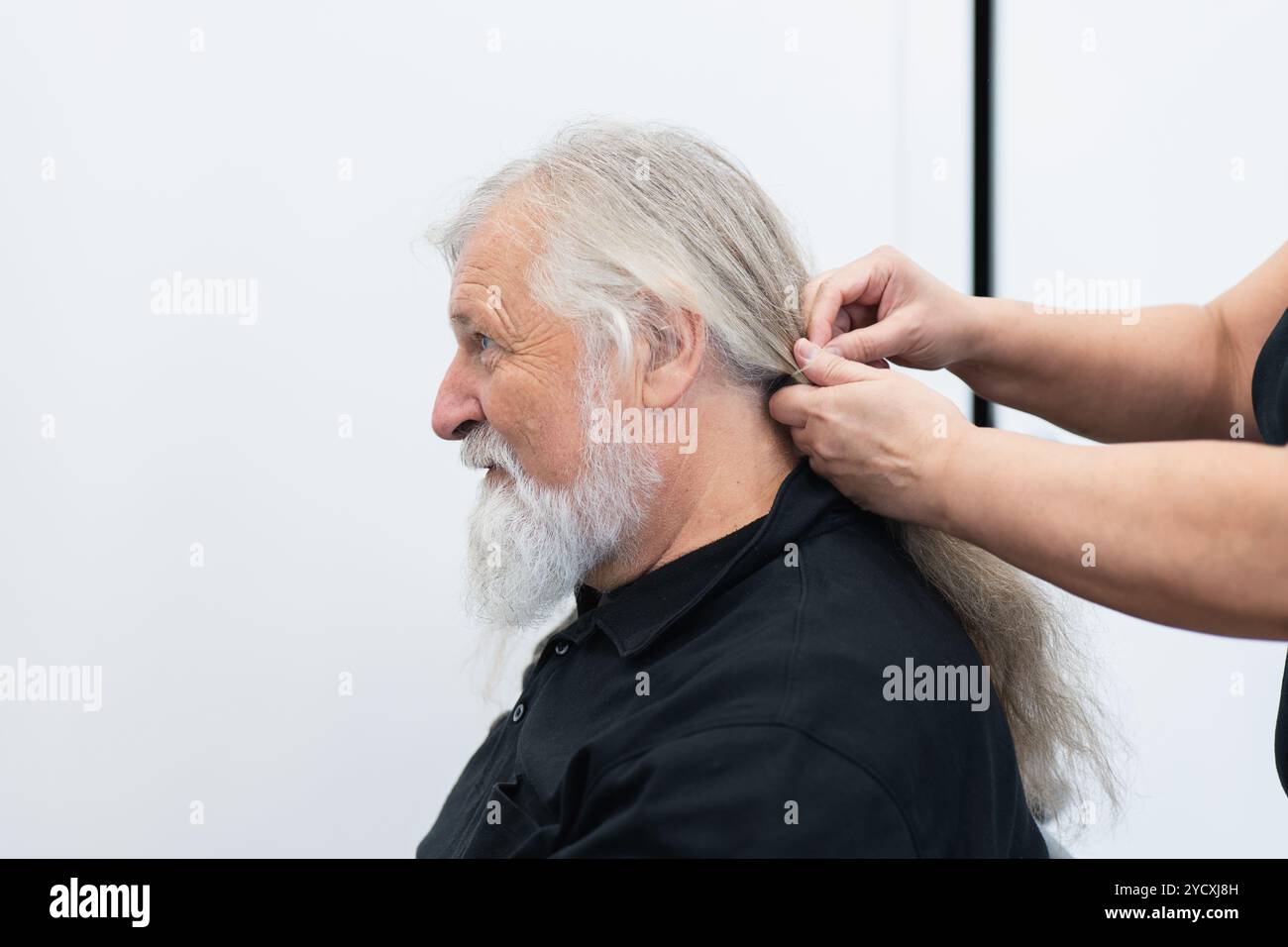 Un homme âgé avec une longue barbe grise sourit alors qu'une femme rassemble ses longs cheveux gris, les préparant pour un don Banque D'Images
