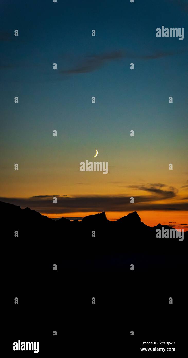 Un magnifique croissant de lune pend dans le ciel crépusculaire au-dessus de la silhouette des Alpes suisses, avec un coucher de soleil coloré illuminant l'horizon près du lac Ge Banque D'Images