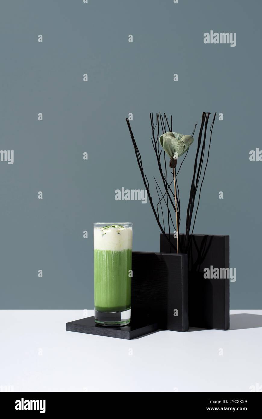 Un élégant verre de thé matcha froid surmonté de crème fouettée, sur un fond gris contemporain avec un décor artistique. Banque D'Images