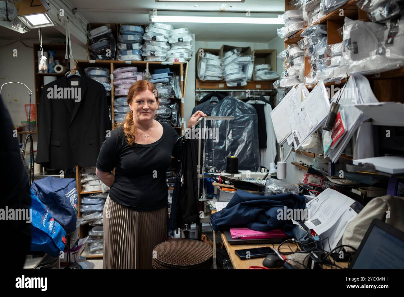 Femme debout dans les transformations et le back office d'un magasin de vêtements pour hommes à St Albans dans le Hertfordshire, Angleterre, Royaume-Uni Banque D'Images