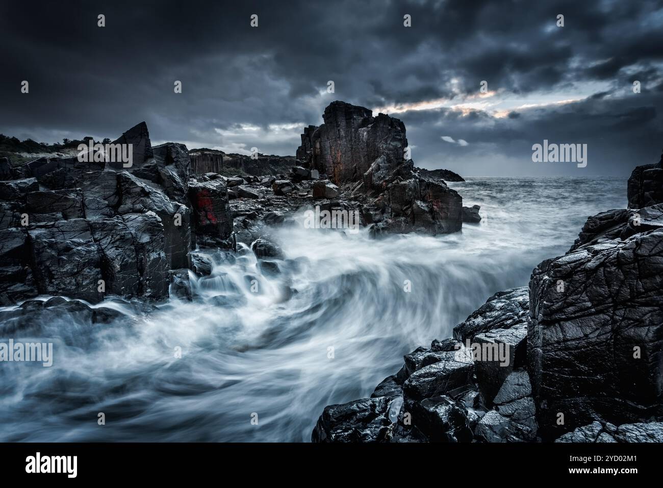 Des cieux dramatiques et de grandes vagues s'écrasent sur les rochers côtiers Banque D'Images