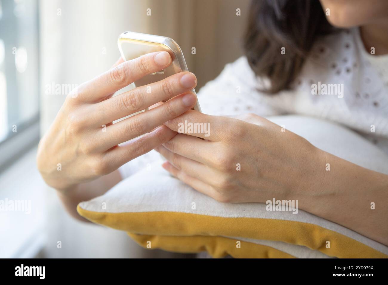 Une femme est assise réfléchie tout en tenant un smartphone, son attention concentrée sur l'écran. Banque D'Images