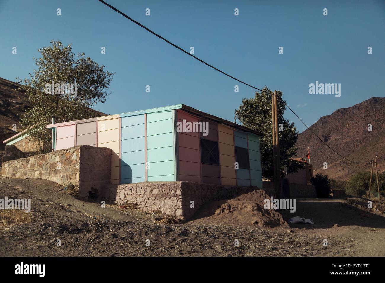 Une maison au design unique avec une façade pastel se trouve sur une colline au Maroc, entourée d'arbres et d'un terrain naturel, mettant en valeur le mélange du moderne Banque D'Images