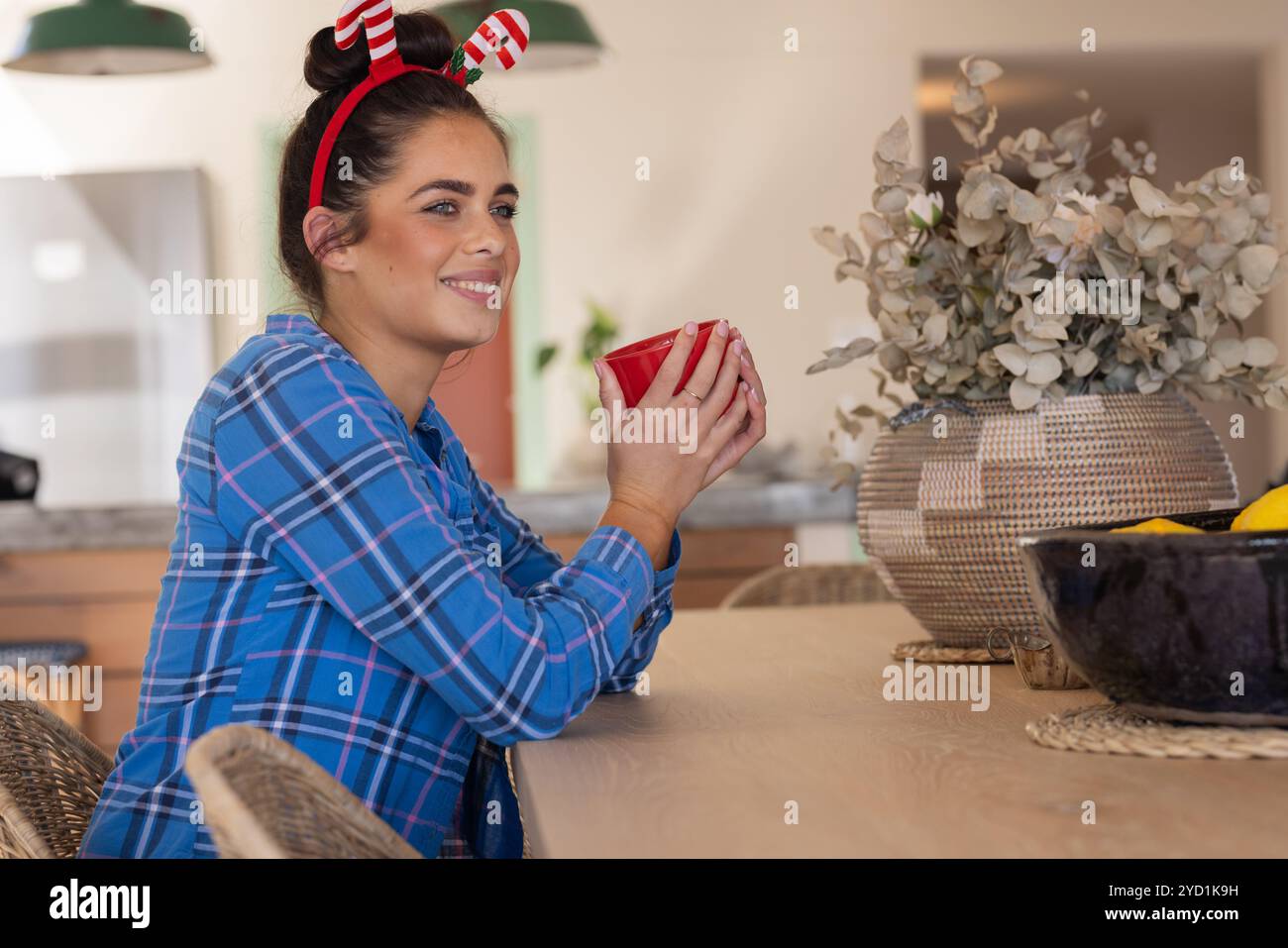 Temps de Noël, femme souriante avec bandeau festif appréciant la boisson chaude à la table de cuisine Banque D'Images