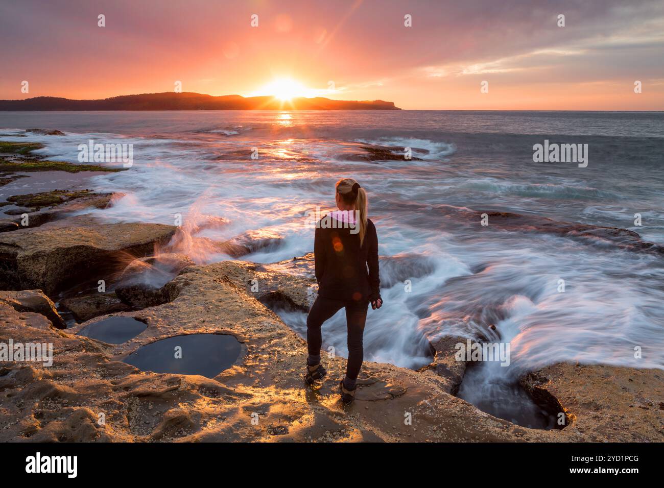 Sunflare embrassant l'épaule d'une femme regardant le lever du soleil près de l'océan Banque D'Images