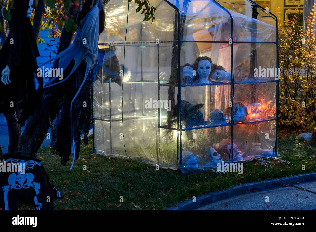 Décorations de maison extérieure pour Halloween avec une serre remplie de masques effrayants illuminés la nuit créant une atmosphère étrange Banque D'Images