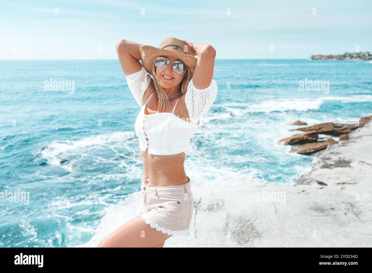 Femme bronzée vivaceuse en short et crop top par l'océan Banque D'Images