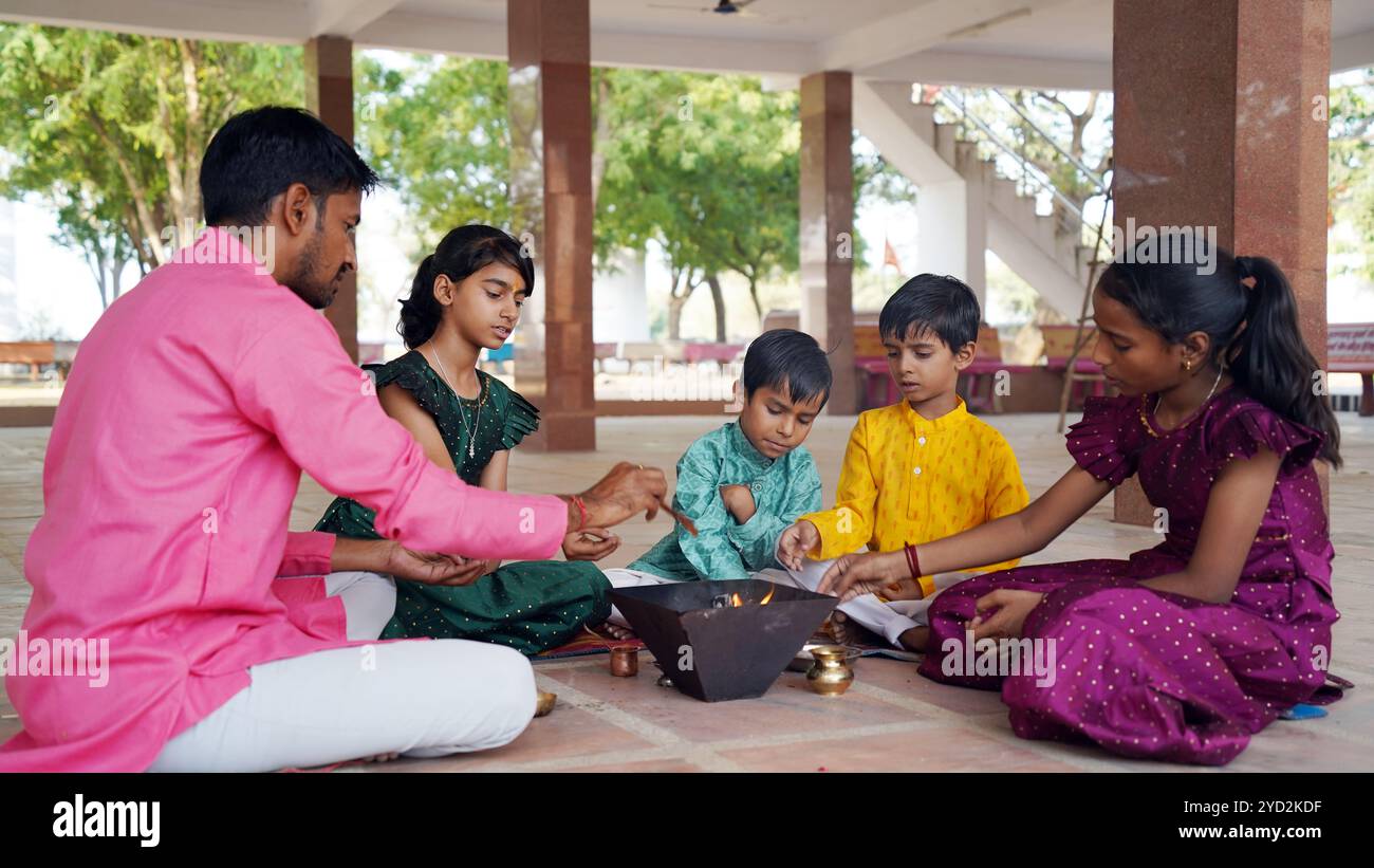 Une famille indienne en tenue traditionnelle exécute un Yagya ou Havan, dirigé par un prêtre, pour équilibrer les énergies dans leur maison. Cette pooja sacrée est pour l'harmonie Banque D'Images