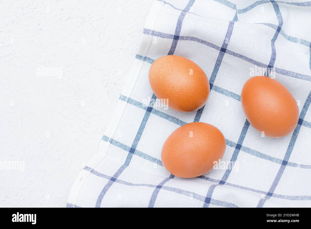 Oeufs de poule sur une serviette de cuisine à carreaux sur une table lumineuse. concept de produits agricoles et d'aliments naturels. Article sur les produits pour la maison Banque D'Images