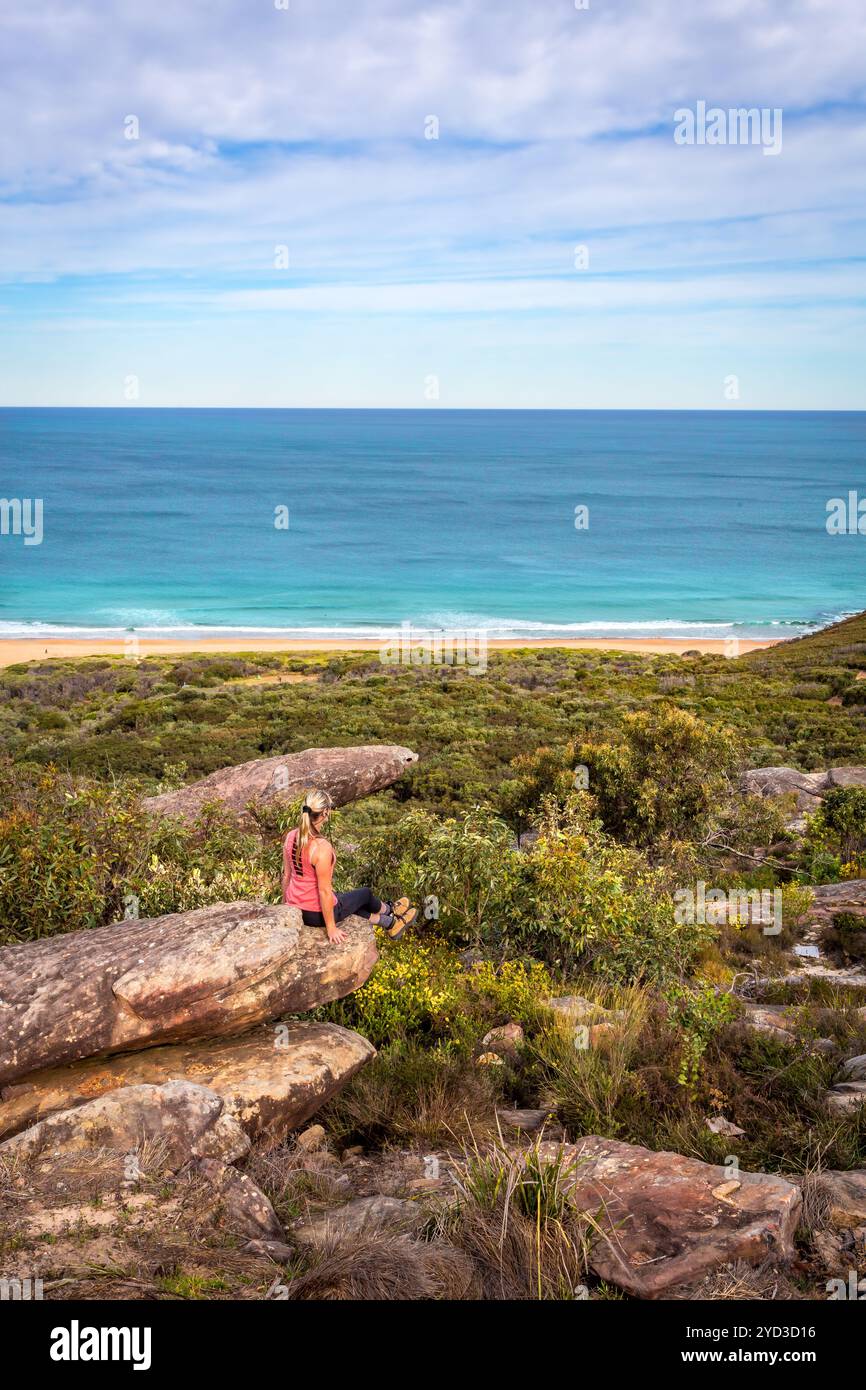 Femme assise sur des rochers en vêtements actifs avec vue sur la plage et l'océan Banque D'Images