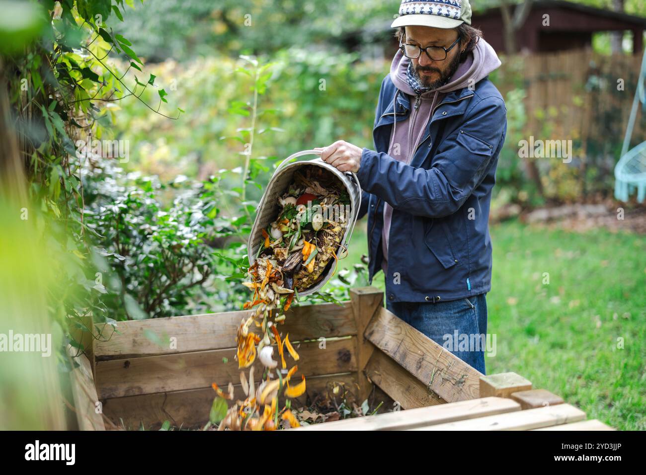 Homme jetant des restes de légumes dans un récipient de compost dans la cour arrière Banque D'Images