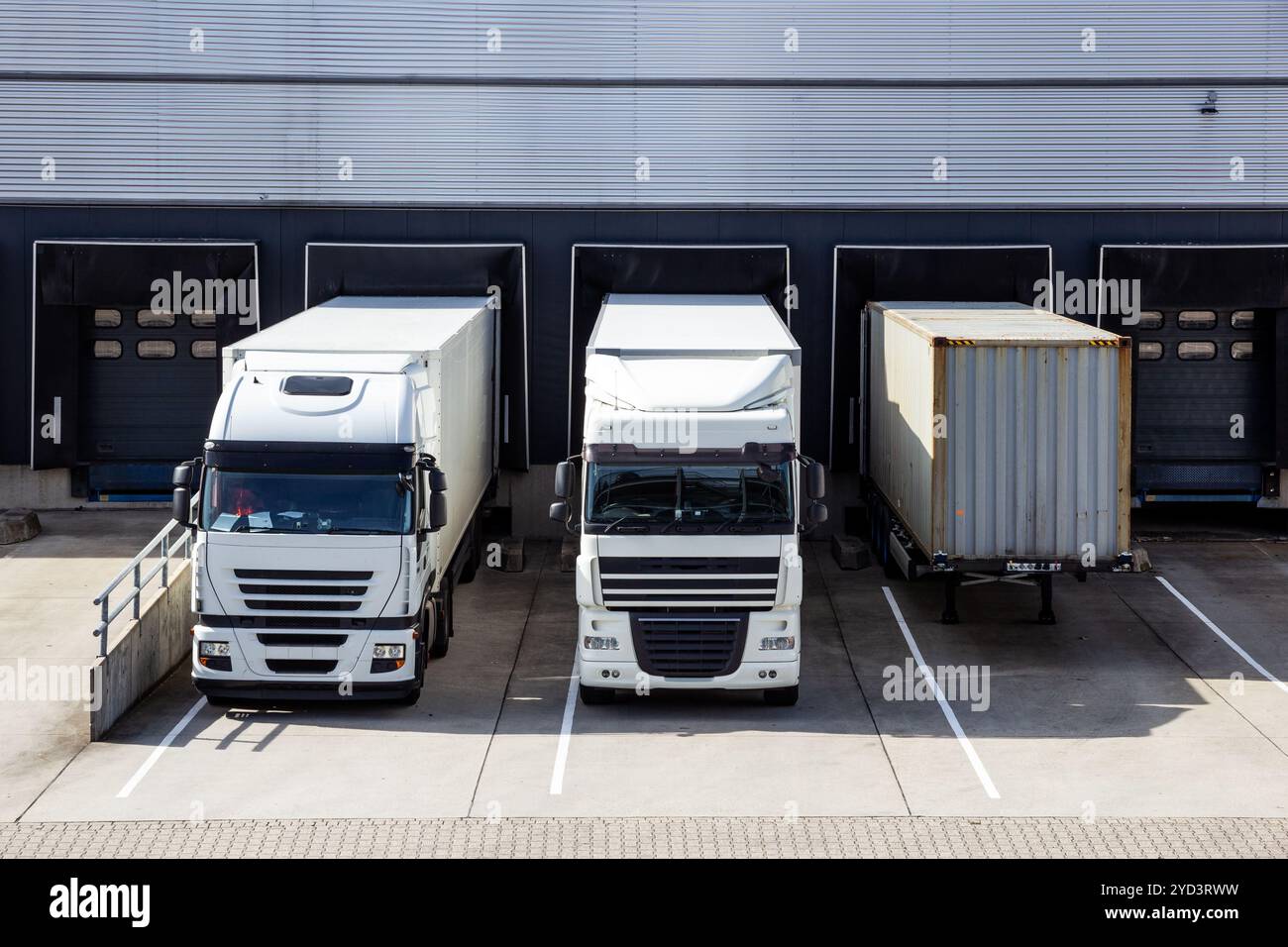 Camions et remorques devant une rangée de quais de chargement avec portes à volets dans un entrepôt industriel. Banque D'Images