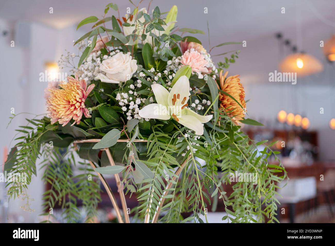 Pièce maîtresse florale sur un grand stand doré sur une table dans un restaurant affichant un élégant mélange de lys blancs, chrysanthèmes de pêche doux et de feuilles Banque D'Images