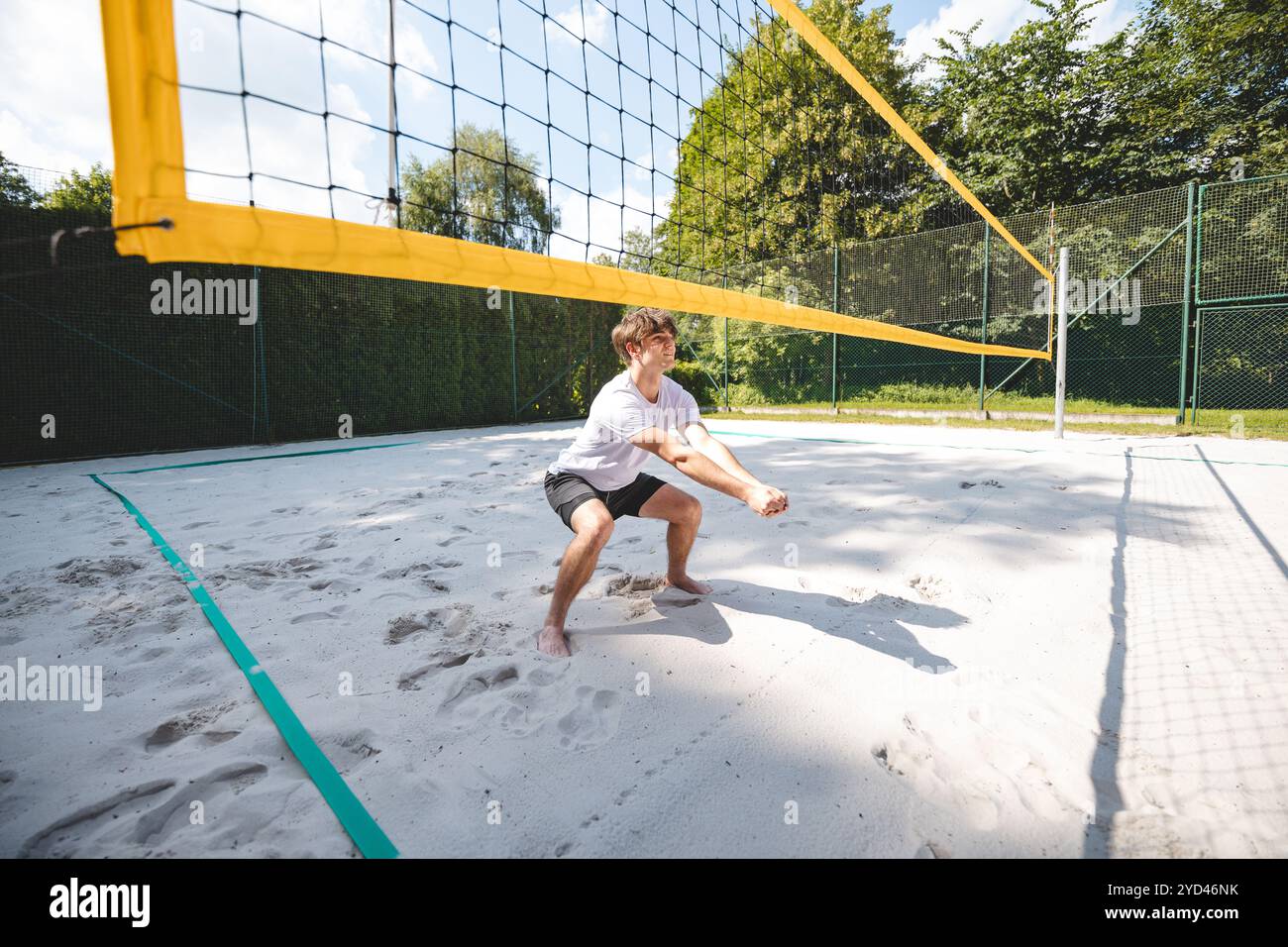 Jeune homme dans une position prête, se préparant à recevoir ou à creuser un volley sur un terrain de sable. Capturer l'intensité et la concentration du Beach volley dans un Banque D'Images