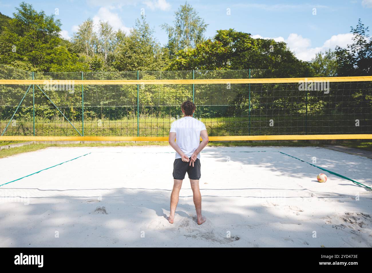 Joueur de volley-ball debout sur un terrain de volley-ball de sable, les mains derrière son dos, se préparant pour le prochain match. Un moment de calme au milieu d'un v extérieur Banque D'Images