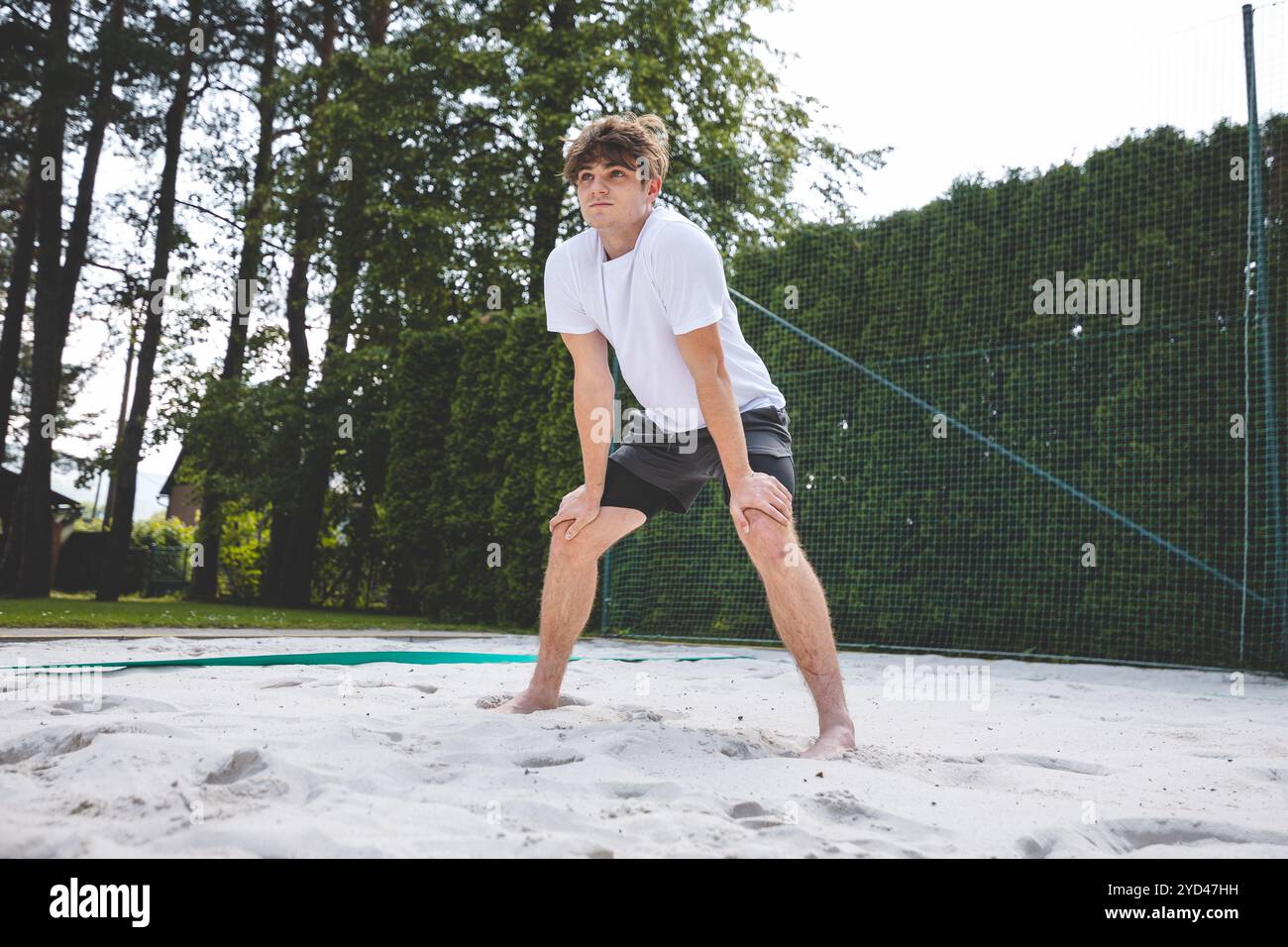 Jeune homme dans une position prête, se préparant à recevoir ou à creuser un volley sur un terrain de sable. Capturer l'intensité et la concentration du Beach volley dans un Banque D'Images