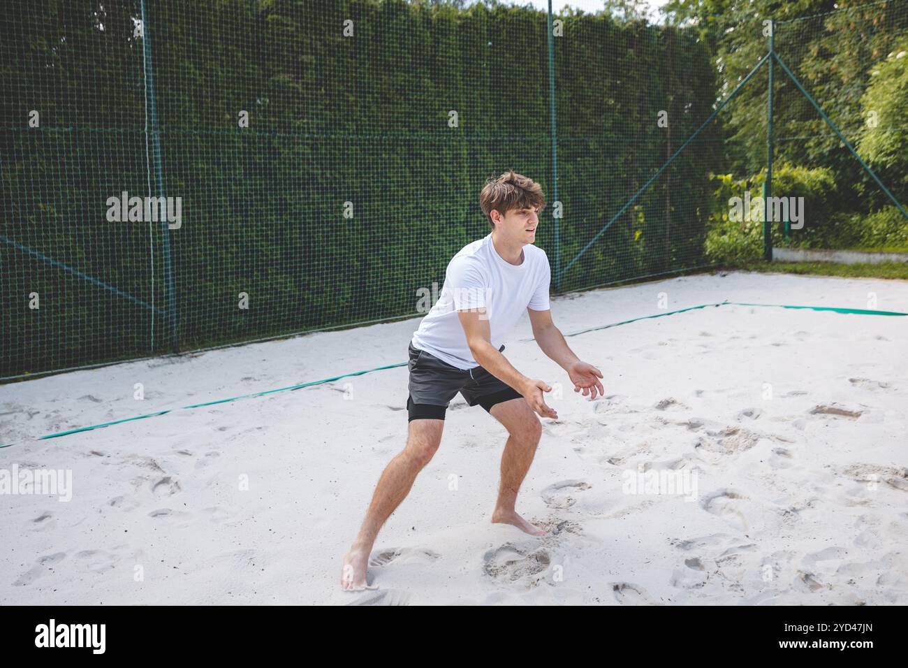 Jeune homme dans une position prête, se préparant à recevoir ou à creuser un volley sur un terrain de sable. Capturer l'intensité et la concentration du Beach volley dans un Banque D'Images