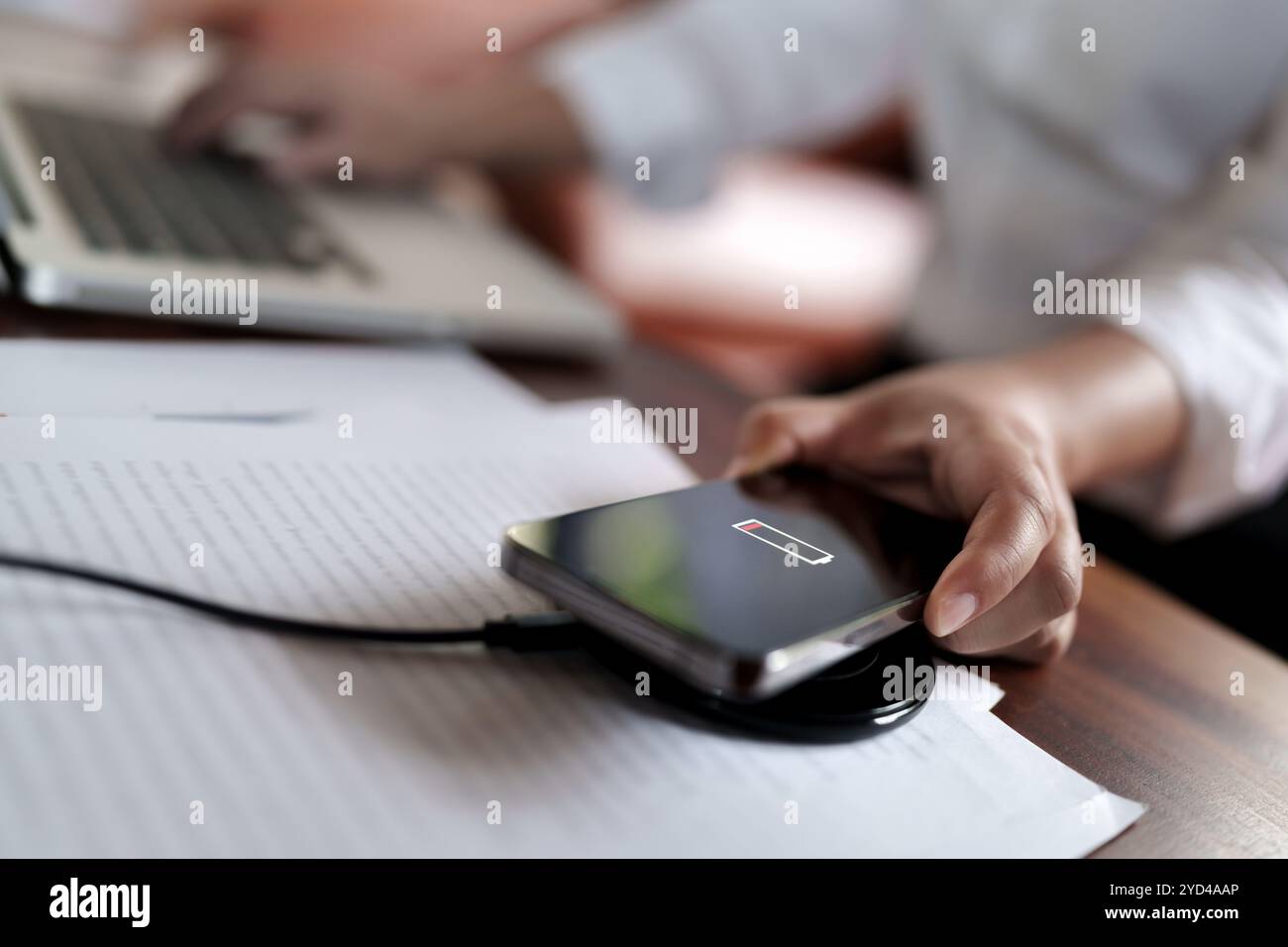 Femme chargeant le téléphone mobile avec le pad de chargeur rapide sans fil sur le bureau. Banque D'Images