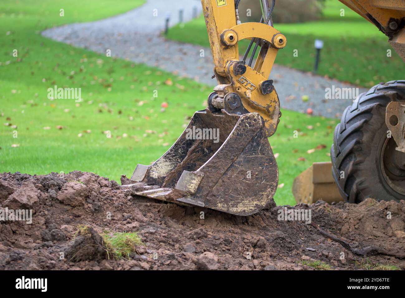 Chantier de construction avec une pelle jaune creusant le sol dans une zone de parc herbeux, idéal pour les projets impliquant l'aménagement paysager, le terrassement, le développement Banque D'Images