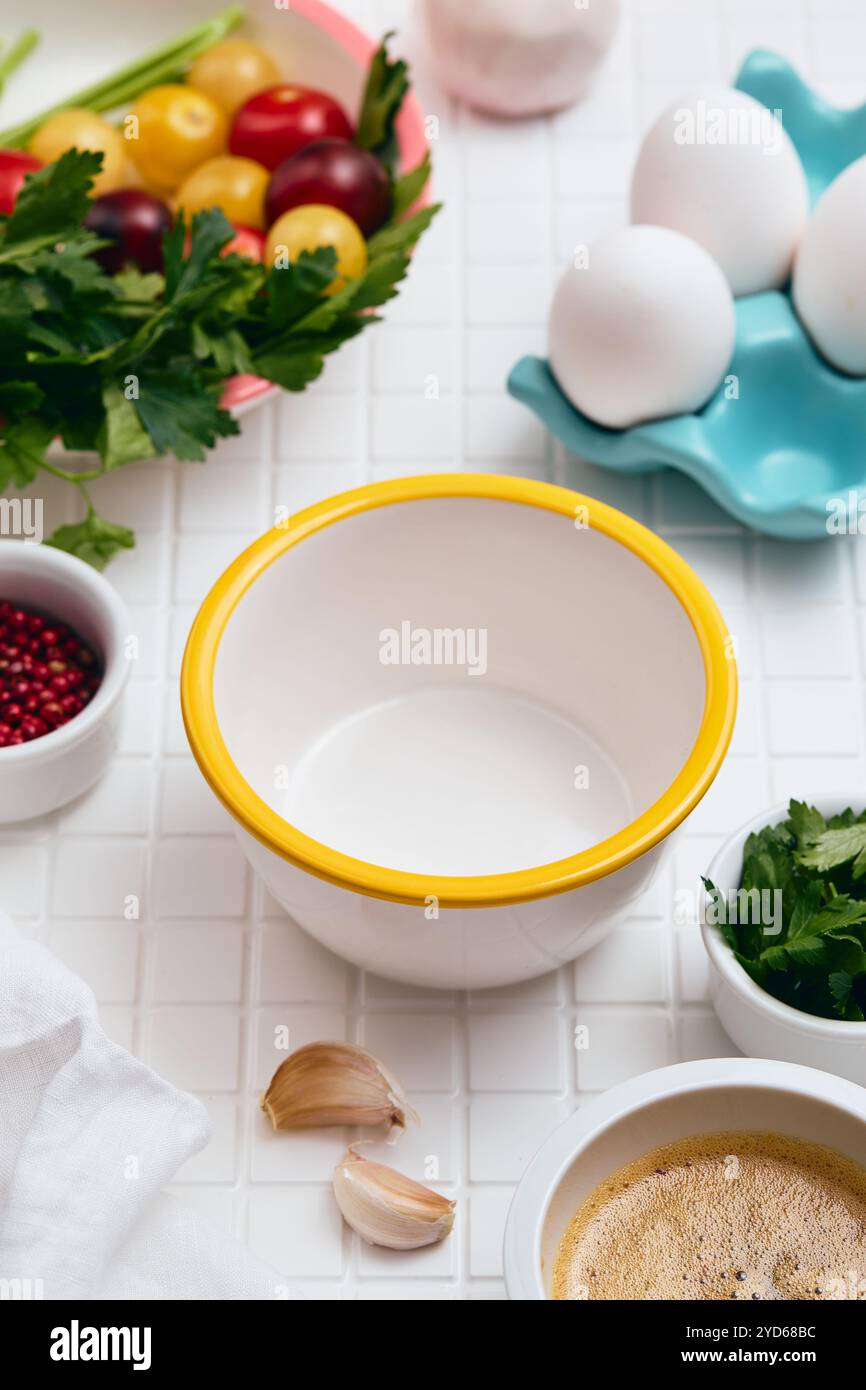 Bol vide blanc avec rebord jaune se trouve sur la table avec d'autres bols et ingrédients. Banque D'Images