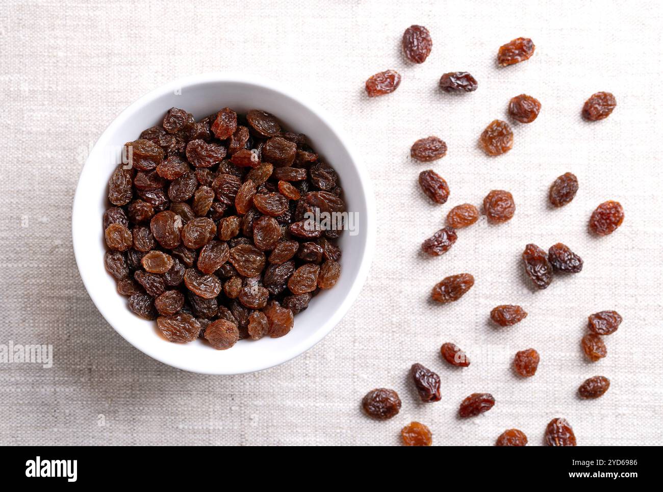 Raisins secs commerciaux communs, dans un bol blanc sur tissu de lin. Grands raisins secs de raisin séchés de couleur foncée, à consommer crus ou utilisés en pâtisserie. Banque D'Images