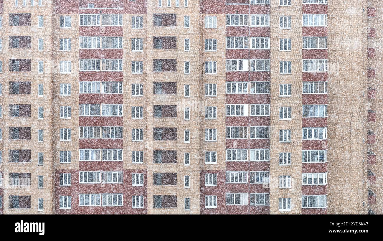 L'heure d'hiver détaille de nombreuses fenêtres dans la construction de briques et la neige tombe. Cadres de fenêtres de ville dans une maison d'habitation Banque D'Images