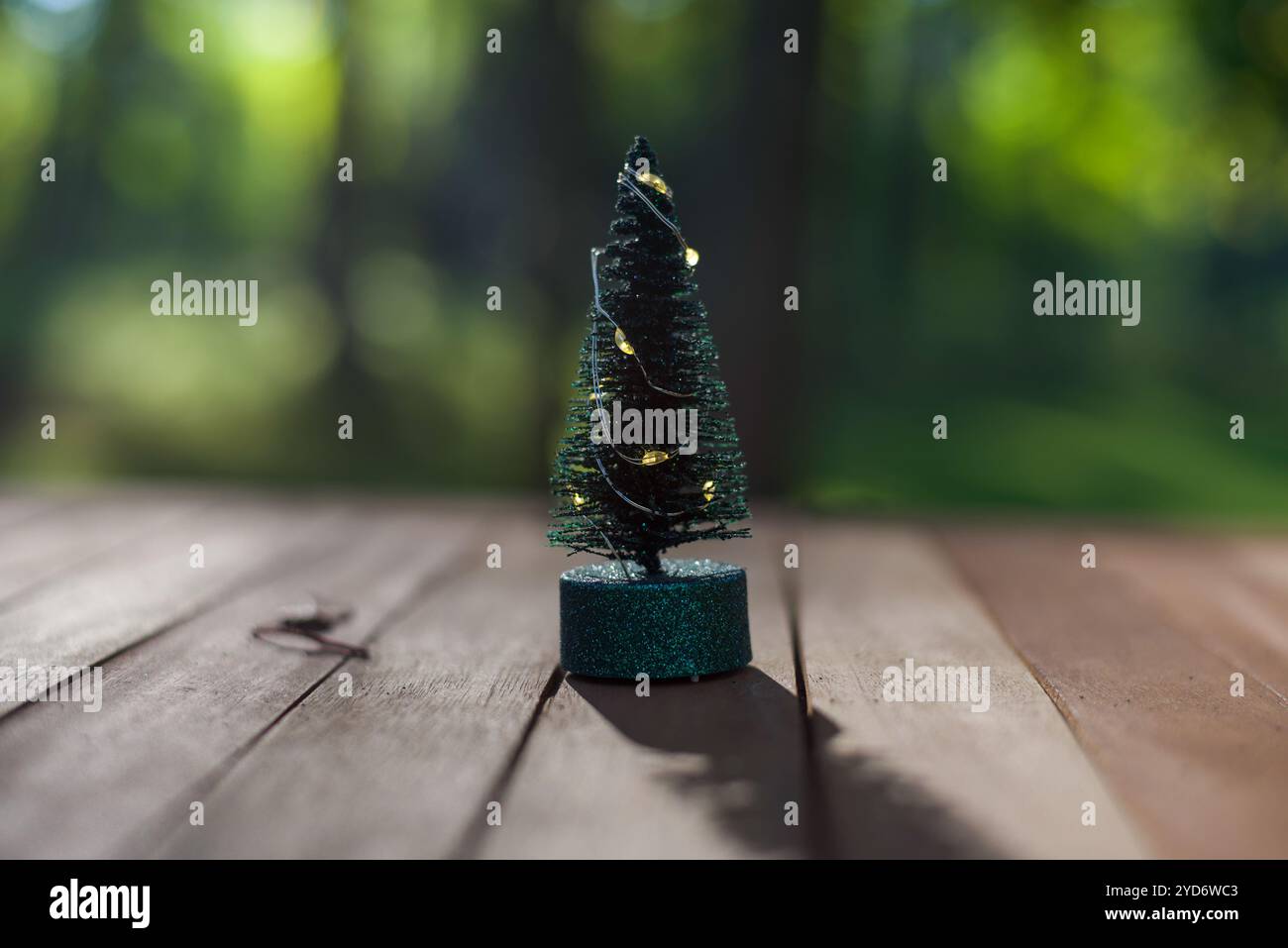 Un mini sapin de Noël avec des lumières de fée debout sur une table en bois avec un beau fond bokeh d'arbre. copier l'espace Banque D'Images