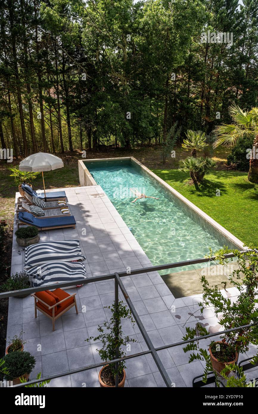 Chaises longues au bord de la piscine avec personne nageant dans une villa de luxe dans le sud de la France. Banque D'Images