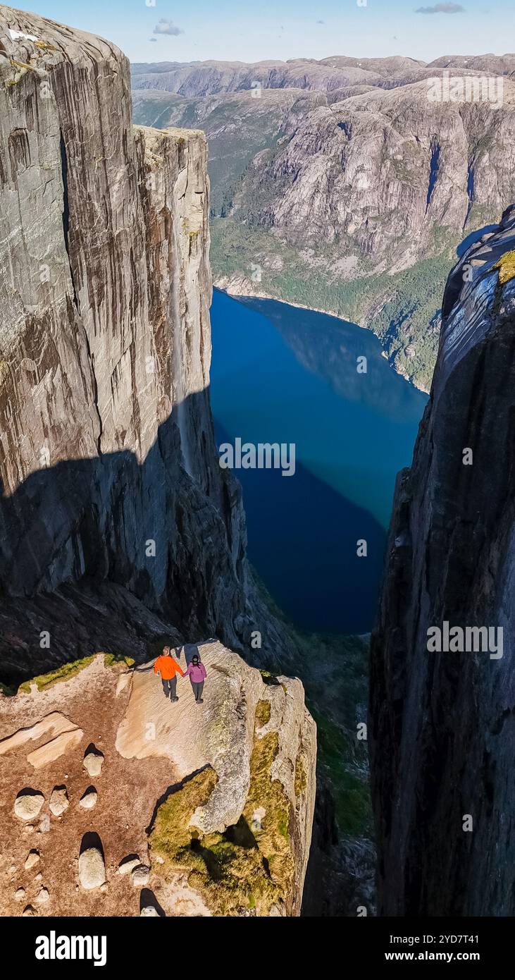 Deux randonneurs se tiennent au bord de Kjeragbolten, en Norvège, une falaise spectaculaire en Norvège, surplombant un magnifique fjord bleu Banque D'Images