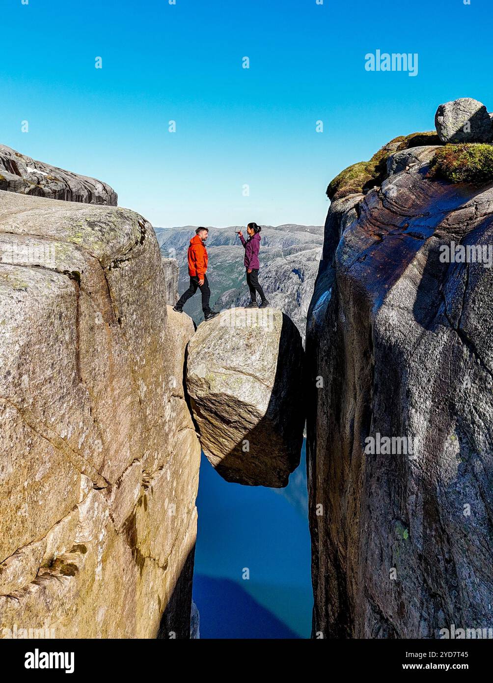 Kjeragbolten, Norvège, deux personnes se tiennent debout sur un pont rocheux surplombant un magnifique paysage norvégien, apparemment suspendu à mi-parcours Banque D'Images