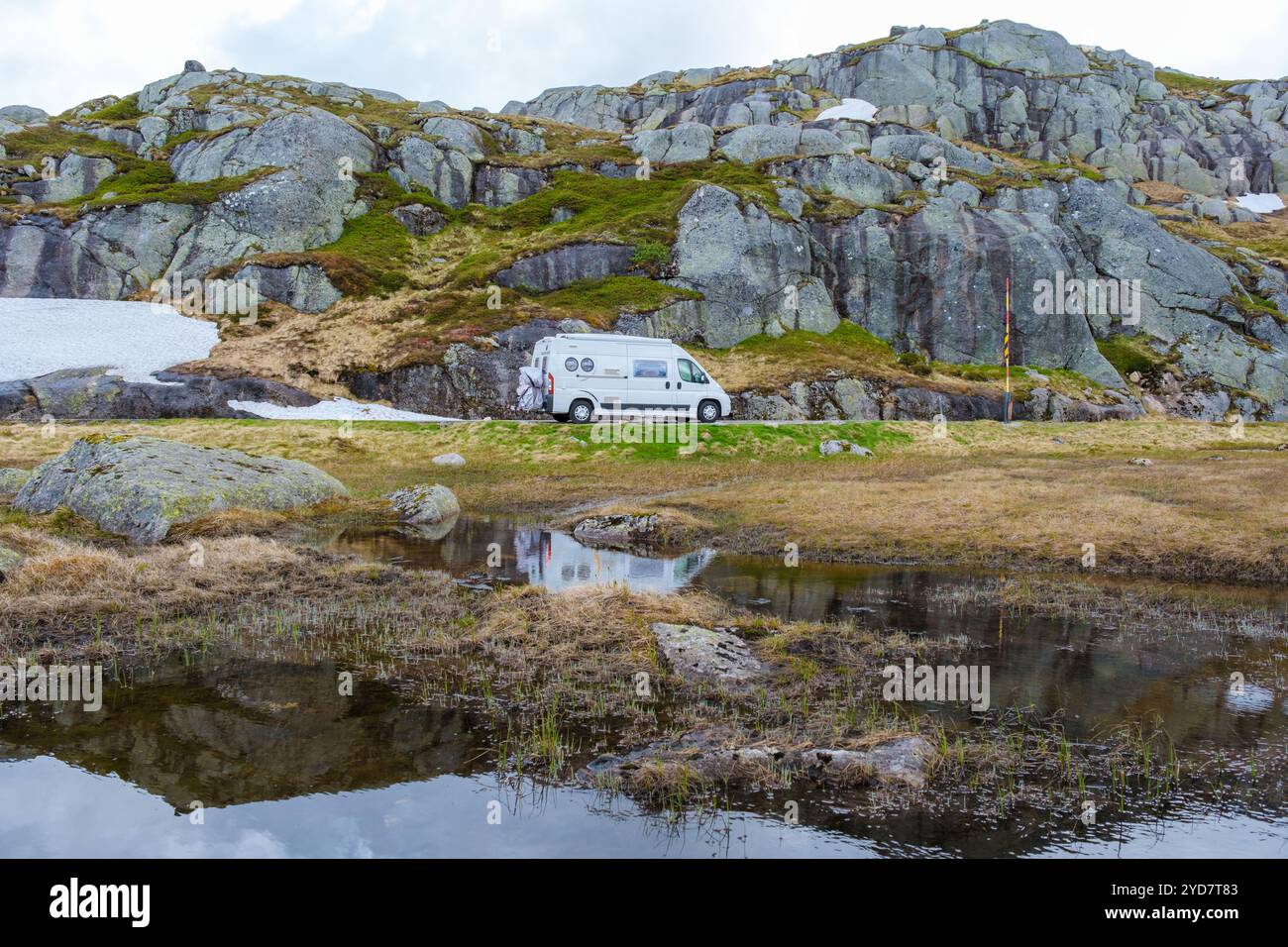 Un camping-car blanc est garé sur une route de montagne en Norvège, avec un reflet du van dans un petit étang au premier plan Banque D'Images