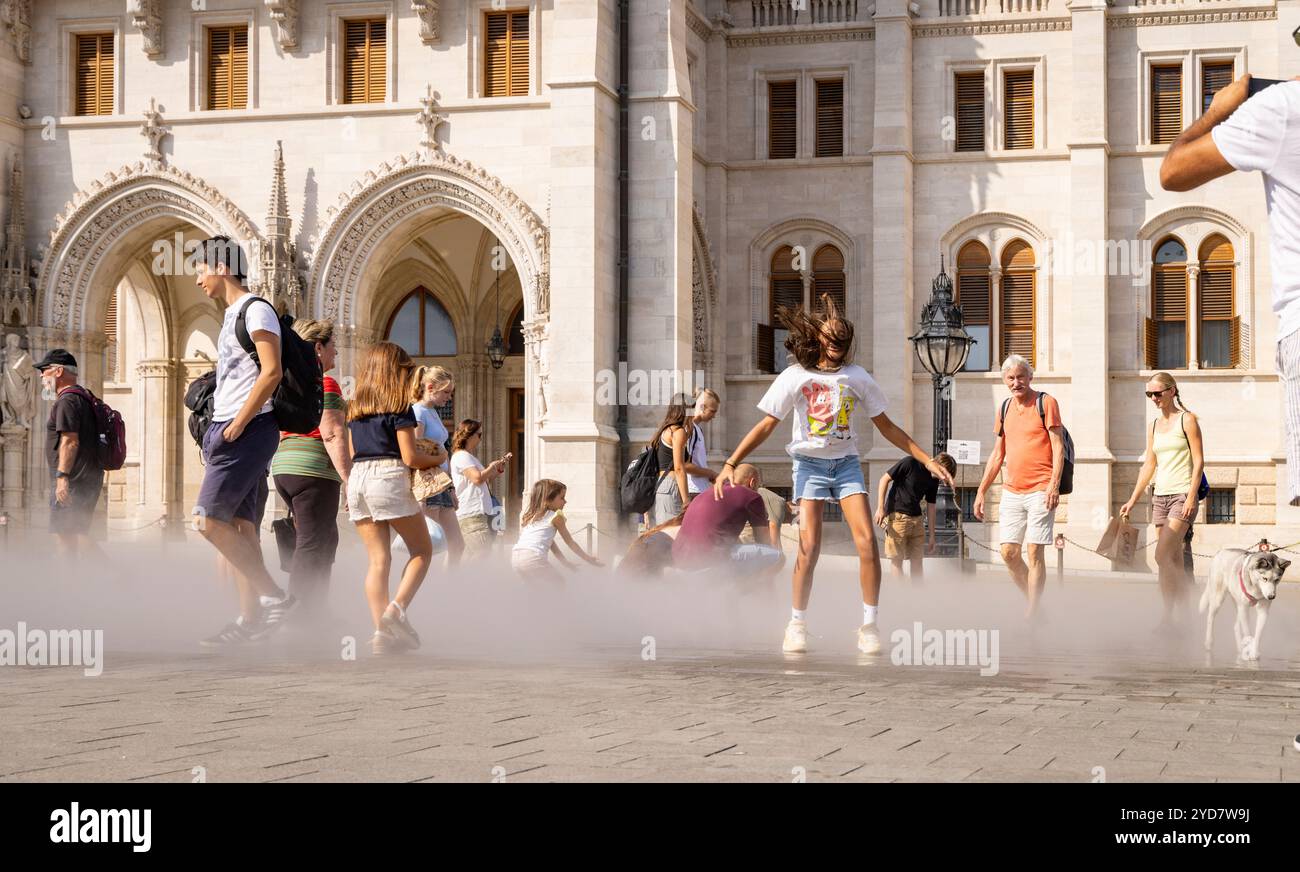 Les gens refroidissent dans des gicleurs d'eau devant le bâtiment du Parlement à Budapest, Hongrie. Banque D'Images