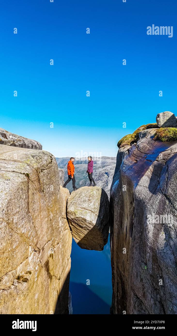 Deux randonneurs se tiennent sur Kjeragbolten, en Norvège, une formation rocheuse surplombant une falaise abrupte en Norvège. Le monument emblématique offre Banque D'Images