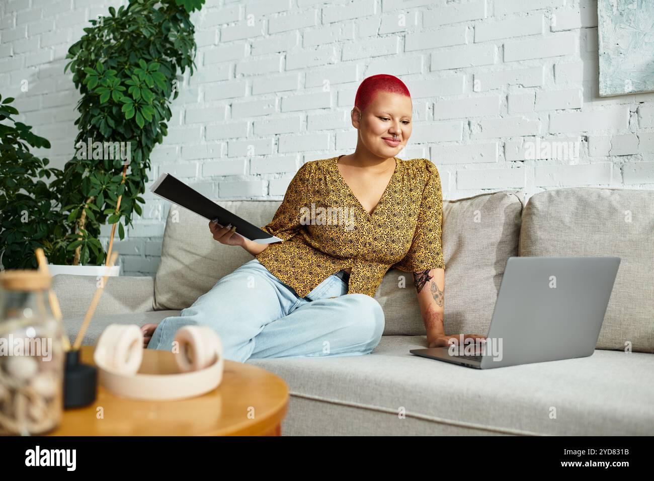 Une femme chauve confiante avec une coupe de pixie rouge utilise son ordinateur portable dans une maison élégante. Banque D'Images