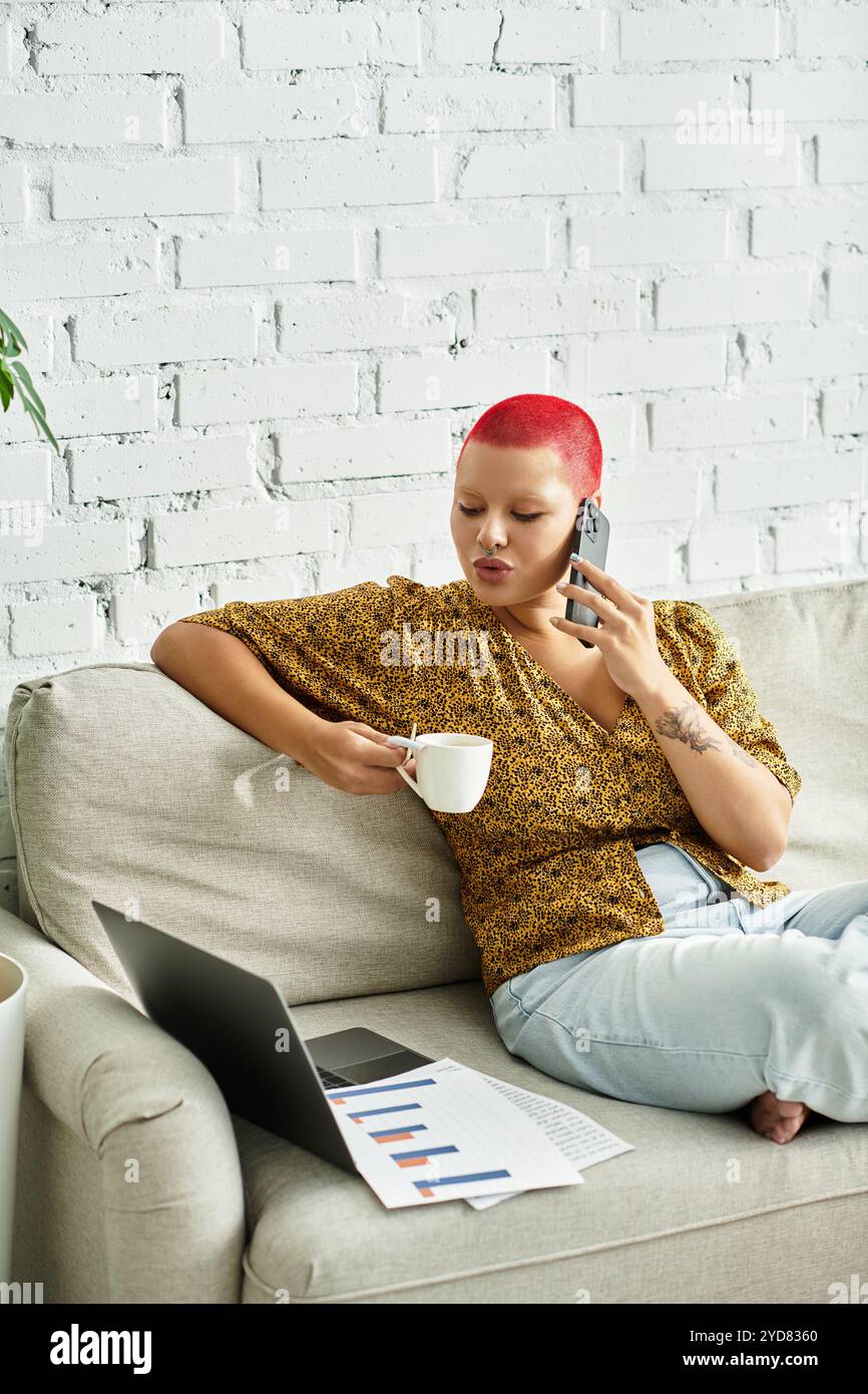 La femme se détend sur le canapé, sirotant un café et engagée dans une conversation téléphonique. Banque D'Images