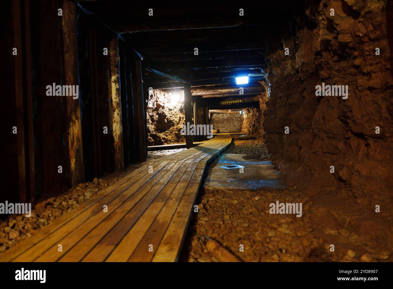 Un tunnel minier sombre et étroit éclairé par une seule ampoule avec une passerelle en bois usée. Banque D'Images